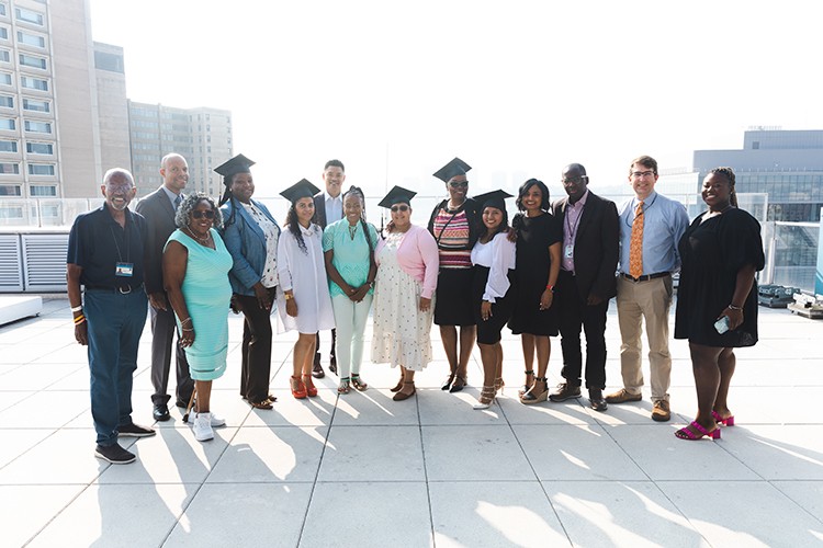 Exterior shot of multiple graduates standing side by side wearing caps while smiling for camera.