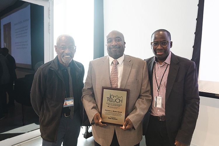 Three gentlemen dressed in suits standing together while smiling for a photo.  Gentlemen in the center holds an InTouch Program Award.