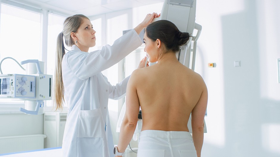 A woman with her back exposed gets help from a healthcare provider as she receives a mammogram screening.