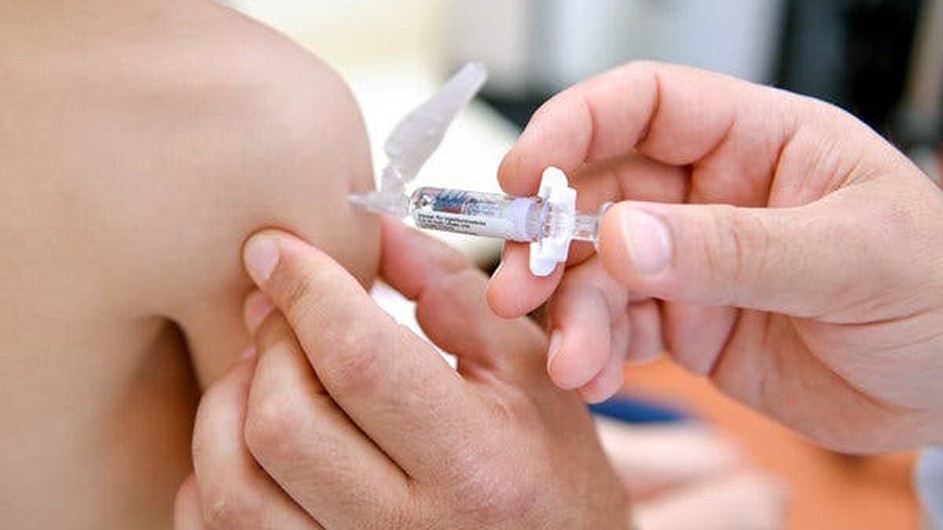 A healthcare professional administers a measles vaccine shot into the arm of a young child.