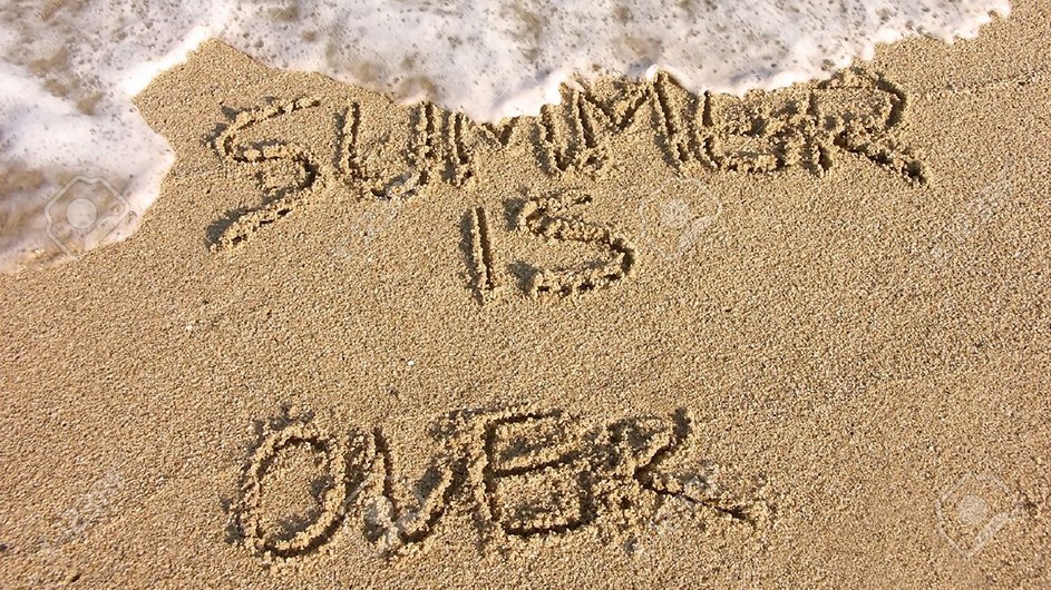A low tide wave washes over the beach where the words "Summer Is Over" are etched into the sand.