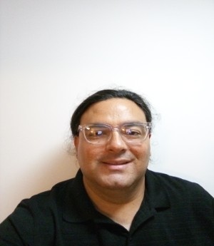 Alexis wears a pair of clear framed eyeglasses and a black button down shirt while smiling into camera. 